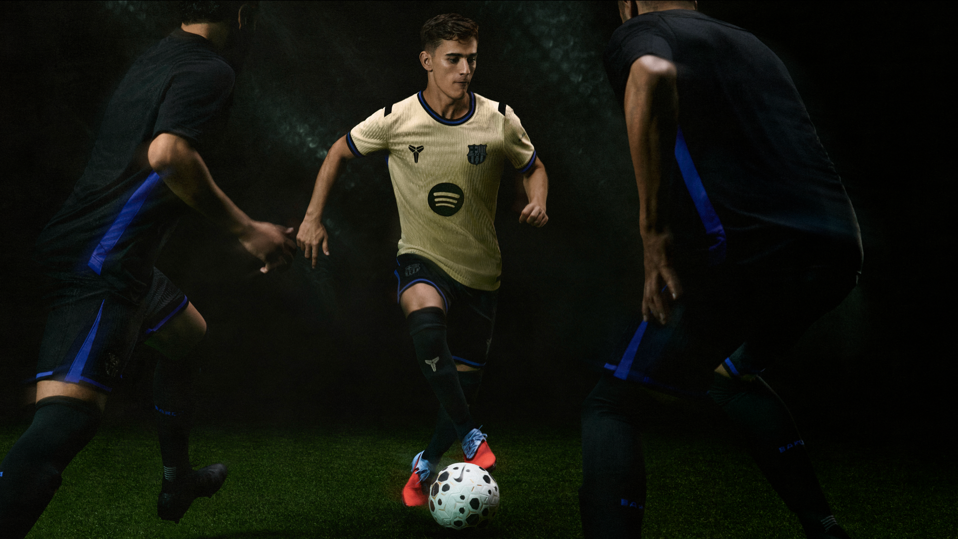 FC Barcelona player in gold kit dribbling between defenders under stadium lights